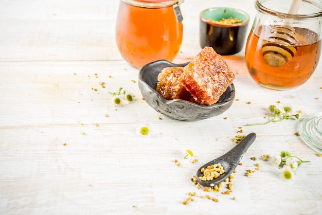 Miel floral bio, en pots, au pollen et aux rayons de miel, sur une table en bois blanche, avec des fleurs sauvages