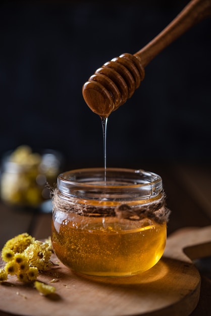 Le miel floral naturel s'écoule dans un pot sur fond de bois. Vue de face