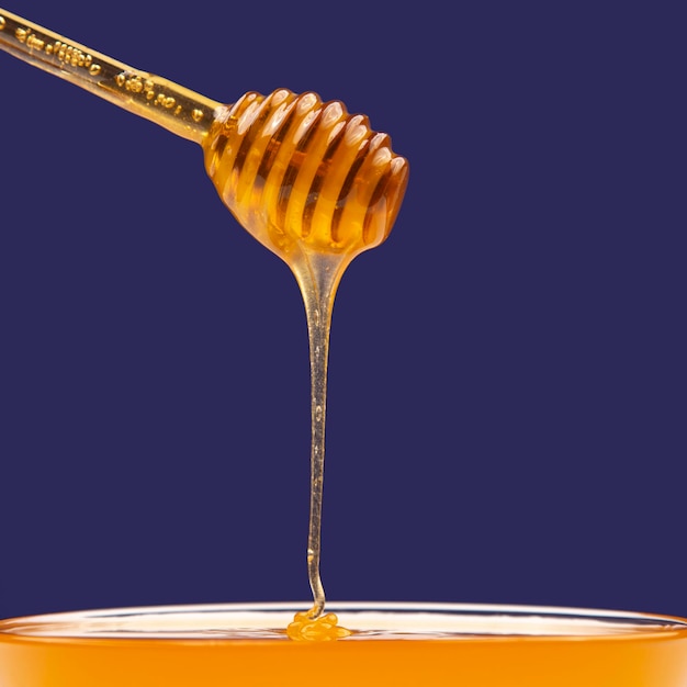 Miel frais dégoulinant d'une cuillère dans une assiette sur fond bleu. aliments santé vitamines biologiques