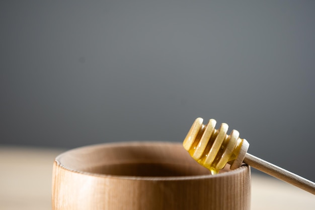 Miel avec louche à miel en bois dans un bol en bois sur une table en bois.