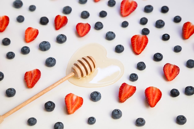 Miel naturel en forme de coeur avec un bâton en bois et avec des myrtilles et des fraises