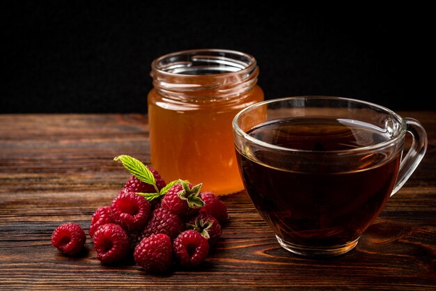 Miel en pot de verre et framboise fraîche sur fond de bois foncé.