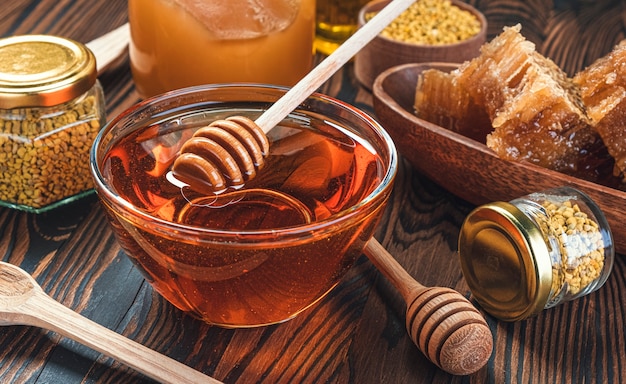 Le miel en pot de verre avec louche de miel sur fond de bois avec nid d'abeille et propolis, sirop de sucre liquide, nectar de fleurs