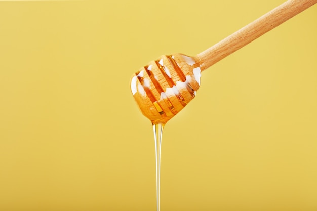 Le miel s'égoutte dans un filet mince d'une louche de miel sur un fond jaune