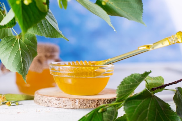 Miel de tilleul en pot et bol avec une louche de miel sur une table en bois blanc