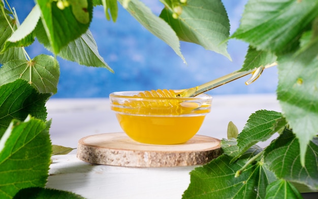 Miel de tilleul en pot et bol avec une louche de miel sur une table en bois blanc