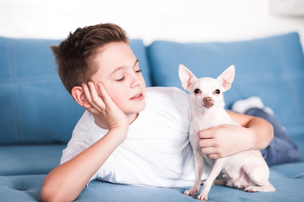 Mignon adolescent garçon tenant un chien chihuhua allongé sur un canapé ensemble à la maison