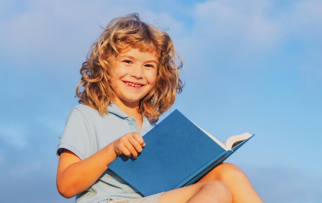 Mignon adorable enfant lisant un livre sur fond de ciel bleu à l'extérieur