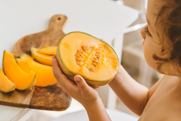 Mignon beau petit garçon mangeant du melon frais.