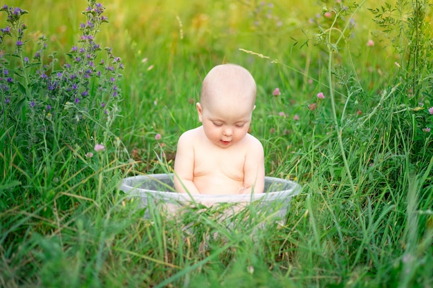 Mignon bébé assis dans un bassin dans l'herbe