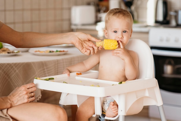 Photo mignon bébé en chaise haute manger du maïs