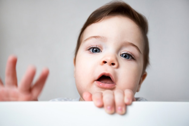 Mignon bébé curieux debout dans un lit de bébé blanc.