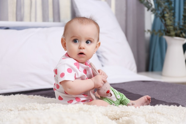 Mignon bébé drôle avec jouet lapin assis sur le lit à la maison