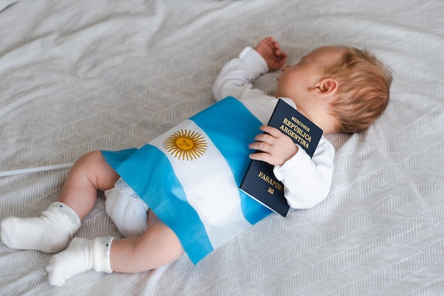 Mignon bébé nouveau-né caucasien sleeplying on bed holding passeport argentin et drapeau concept de ge