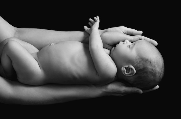 Mignon bébé nouveau-né dans les mains de la mère sur le mur noir