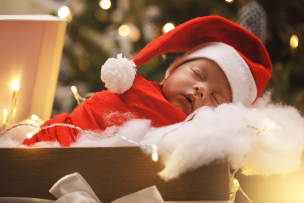 Mignon bébé nouveau-né portant un chapeau de père Noël dort dans la boîte-cadeau de Noël. Joyeux Noel et bonne année.