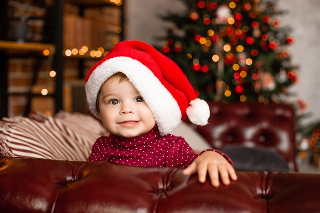 Mignon bébé Père Noël est assis à la maison près de l'arbre de Noël avec des cadeaux