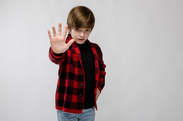 Mignon confiant triste petit garçon caucasien en chemise à carreaux montrant le panneau d'arrêt sur gris