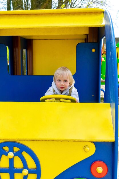 Mignon drôle blond petit jeune enfant en bas âge enfant garçon assis et à cheval dans le train jouet carbus dans la cour de récréationEnfants développement physique et émotionnel et concept de garderie de l'enfance