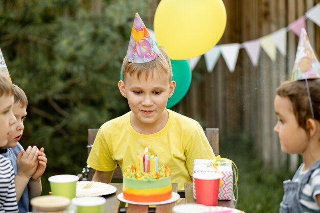 Mignon drôle de garçon de neuf ans célébrant son anniversaire avec sa famille ou ses amis soufflant des bougies sur un gâteau fait maison dans une arrière-cour Fête d'anniversaire pour les enfants