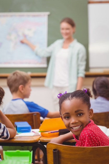 Mignon élève souriant à la caméra à son bureau dans la salle de classe