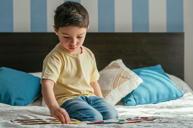 Mignon enfant attentif jouant au jeu de société assis sur le lit