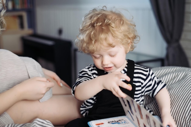 Mignon enfant aux cheveux bouclés un garçon en costume est assis sur un lit avec sa mère et apprend à lire