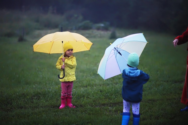 Mignon enfant en bas âge jouant sous la pluie avec un parapluie un jour d'automne brumeux sur une route rurale