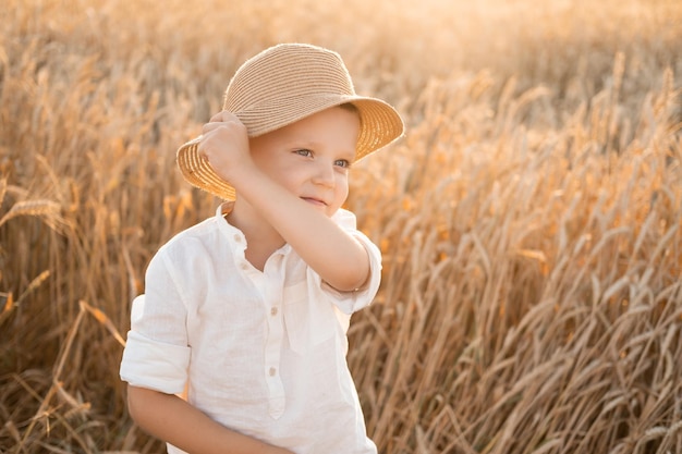 mignon enfant garçon souriant au chapeau de paille s'amusant dans le champ de blé au coucher du soleil d'été concept de base de chalet