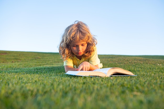 Mignon enfant lisant un livre à l'extérieur sur l'herbe drôle enfant garçon lisant le livre dans le parc du printemps