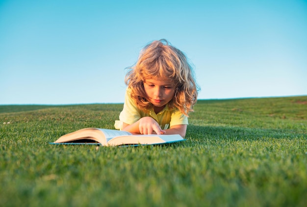 Mignon enfant lisant un livre à l'extérieur sur l'herbe drôle enfant garçon lisant le livre dans le parc du printemps