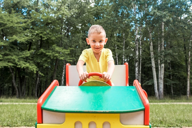 Mignon enfant riant jouant sur une diapositive dans une aire de jeux à l'extérieur sous le soleil d'été.