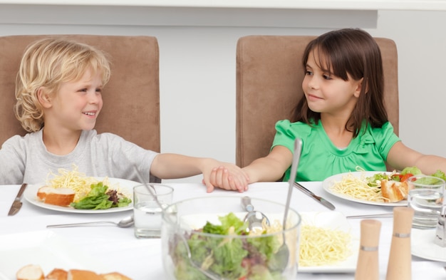 Mignon frère et soeur tenant leurs mains avant le déjeuner