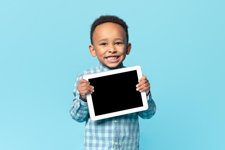 Photo mignon garçon afro-américain tenant une tablette numérique avec un écran noir vierge recommandant une nouvelle maquette d'application ou de site web