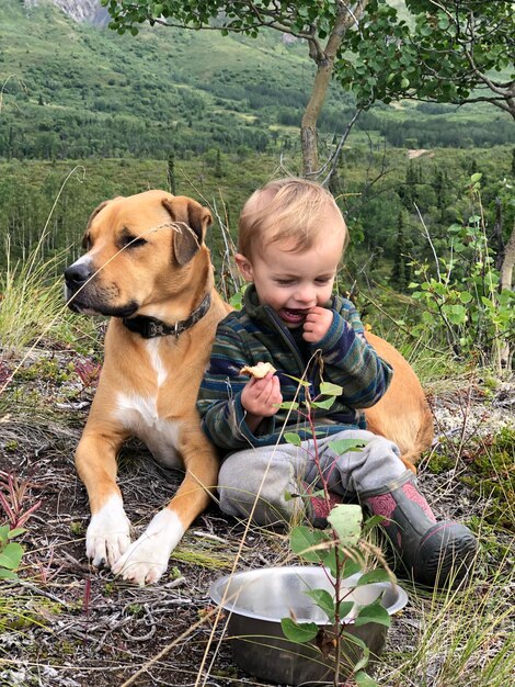 Photo un mignon garçon assis avec un chien sur le terrain.