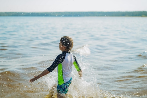 Mignon garçon caucasien courant dans l'eau avec des éclaboussures et des rires Vacances au bord de la mer