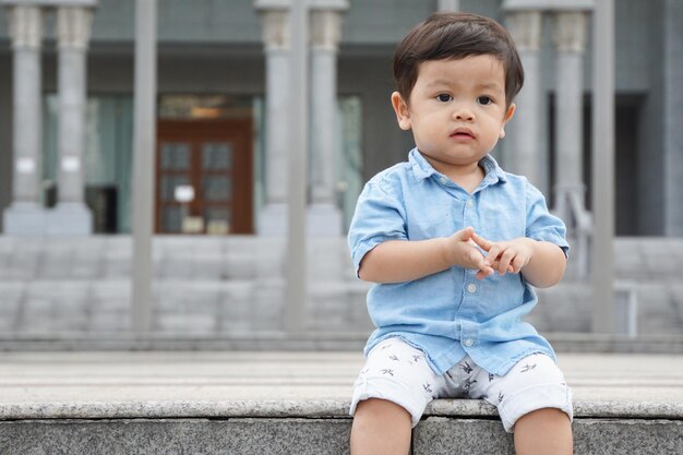Un mignon garçon détournant les yeux alors qu'il est assis à l'extérieur contre le bâtiment.