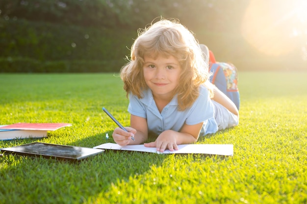 Mignon garçon écrivant des notes dans un cahier portant sur l'herbe sur le pré Enfant lisant un livre en été