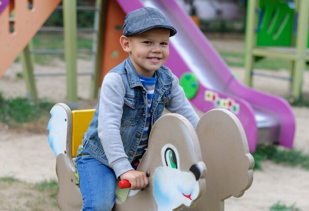 Mignon garçon européen sur l'aire de jeux dans la cour sur une balançoire en été