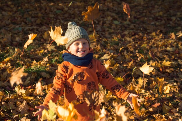 mignon garçon heureux jetant des feuilles d'automne à l'extérieur journée ensoleillée