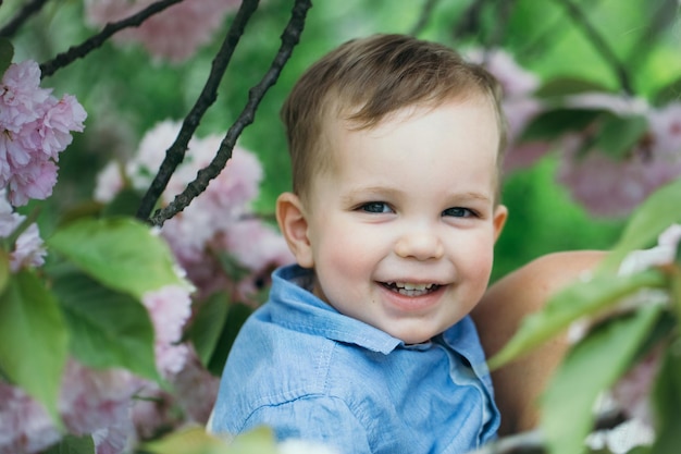 Mignon garçon heureux souriant dans les bras de sa mère parmi les fleurs épanouies