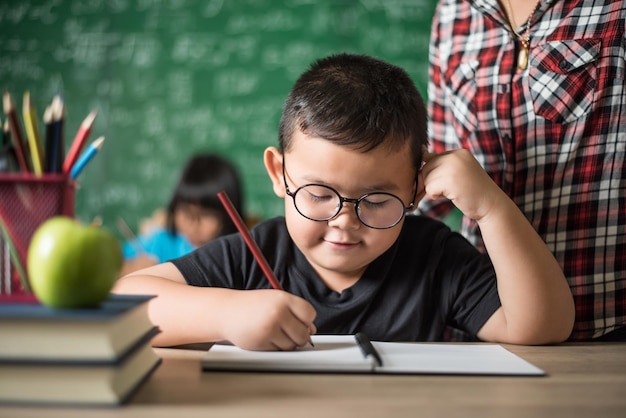 Un mignon garçon avec des lunettes qui étudie contre le tableau noir en classe.