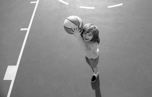 Mignon garçon souriant joue au basket-ball en plein air sur l'aire de jeux enfant tir au basket-ball et jouant b