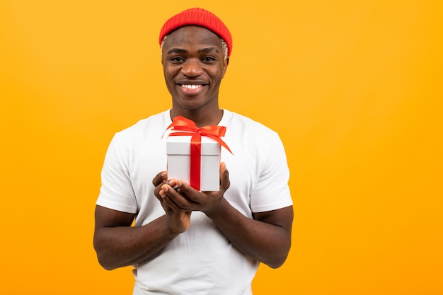 Mignon homme noir américain avec un sourire dans un t-shirt blanc détient une boîte cadeau jaune avec copie espace