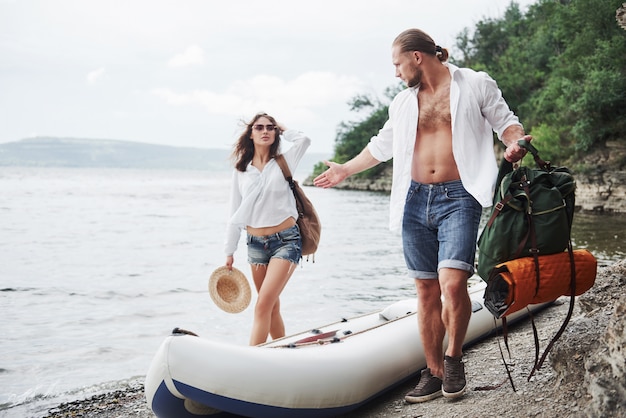 Mignon jeune et couple sur la rivière. Un gars et une femme avec des sacs à dos voyagent en bateau. Concept d'été voyageur