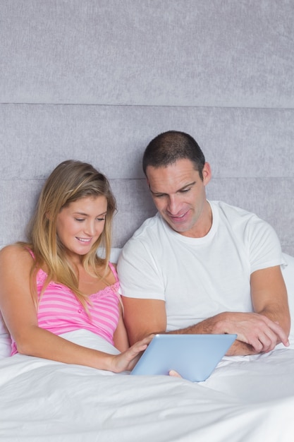 Mignon jeune couple en utilisant leur tablet pc ensemble dans son lit