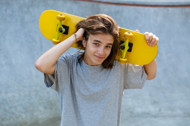 Mignon jeune garçon adolescent, passer du temps au skate park, tenant une planche à roulettes