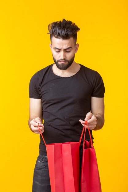 Mignon Jeune Homme Barbu Triste Regarde L'achat Dans Des Sacs à Provisions Sur Une Surface Jaune Avec Copie