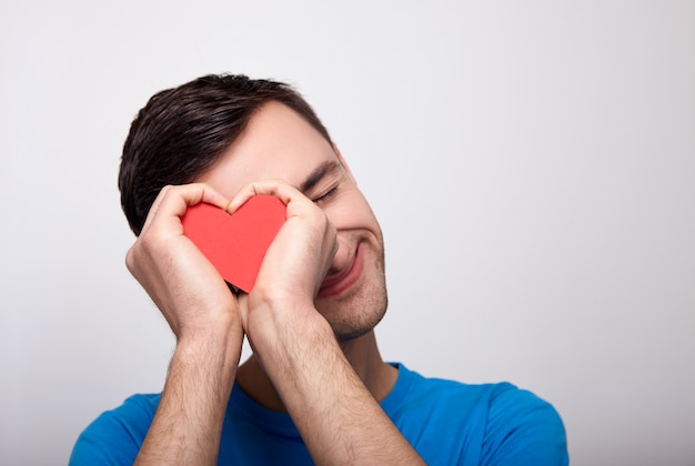 Un mignon jeune homme blanc avec un coeur rouge dans ses mains.