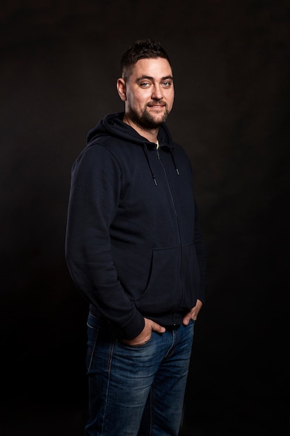 Mignon jeune homme en jeans sur une surface noire. Verticale.